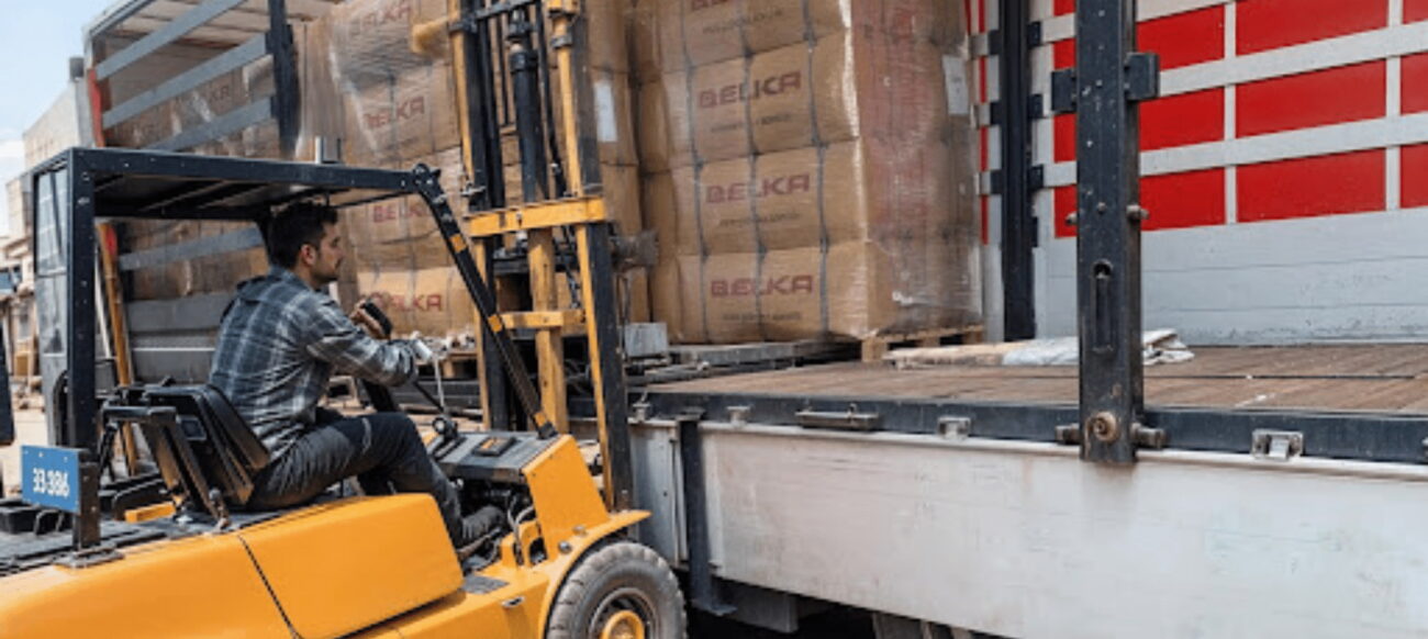 A worker operating a forklift to load pallets of Belka Wallpaper products onto a transport truck.